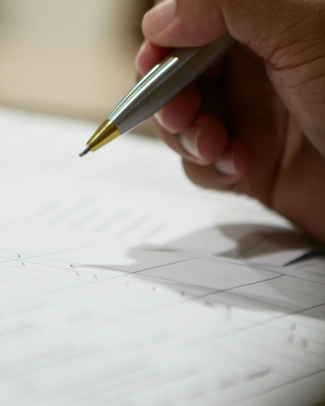 A hand signing a document with a silver pen